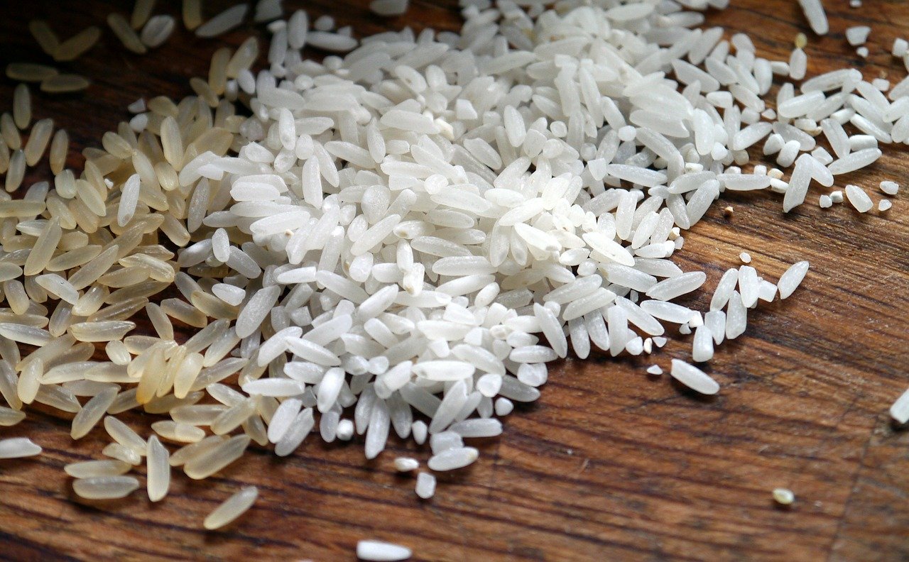 Grãos brancos de arroz espalhados em bandeja de madeira marrom